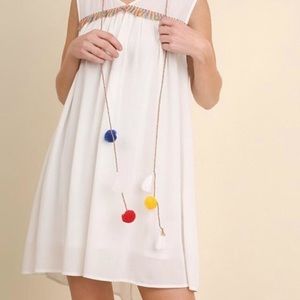 White, flowy dress with colored pom poms.